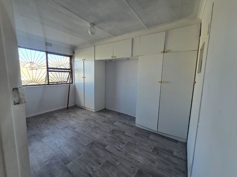 An empty bedroom featuring built-in cupboards, security bars on the window, and grey laminate flooring.