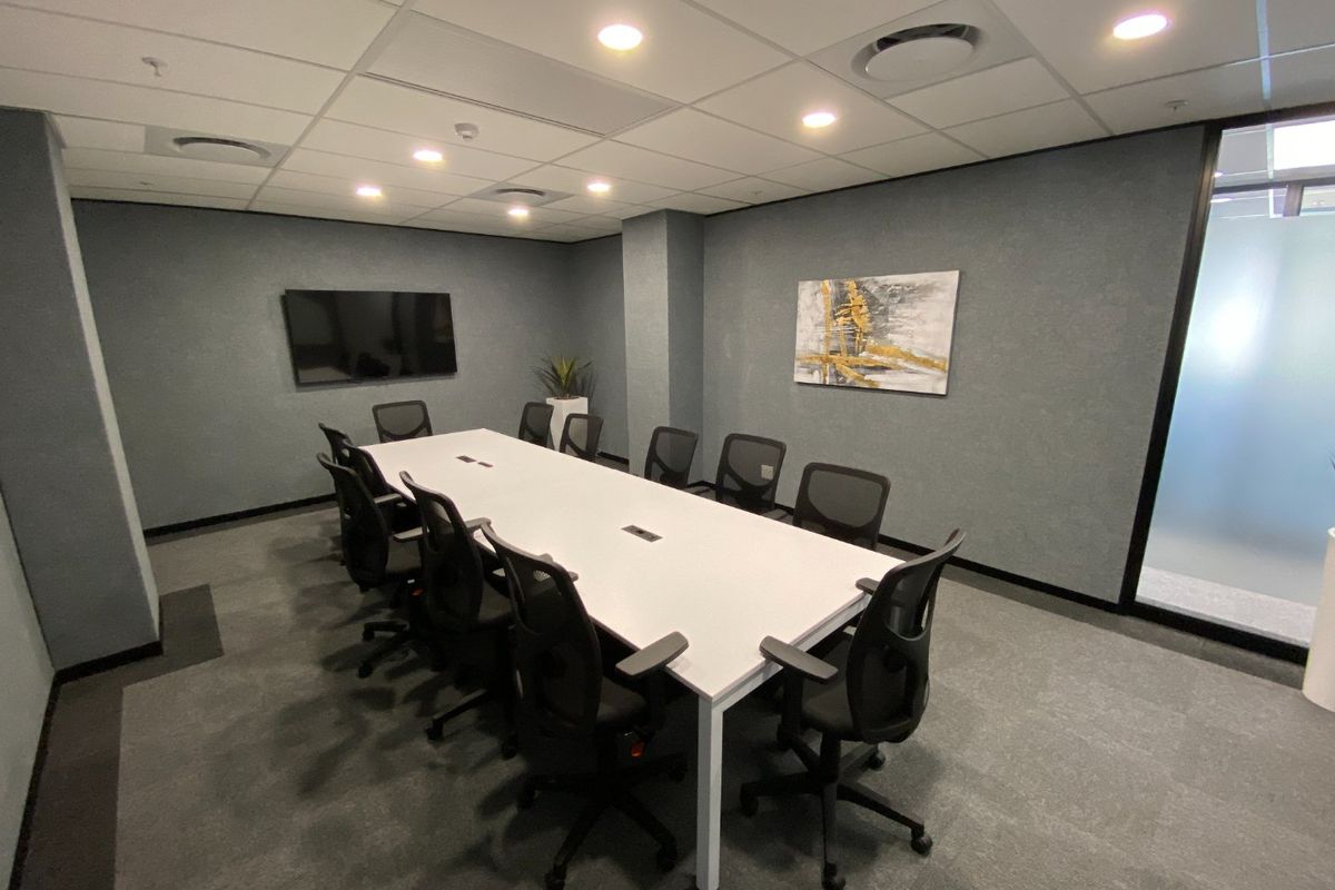 A professional boardroom or meeting room featuring a suspended ceiling with recessed lighting, carpeted flooring, and a modern glass partition wall.