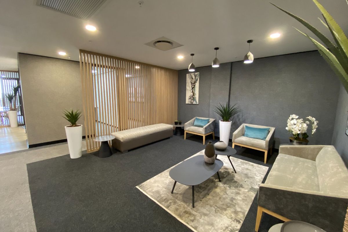 A modern commercial waiting area featuring a timber slat room divider, recessed downlighting, and neutral grey carpeting.