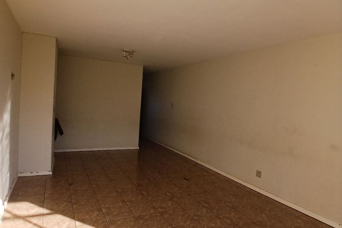 An empty, open-plan living area featuring tiled flooring and basic ceiling lighting, presenting a blank canvas for renovation and interior design.