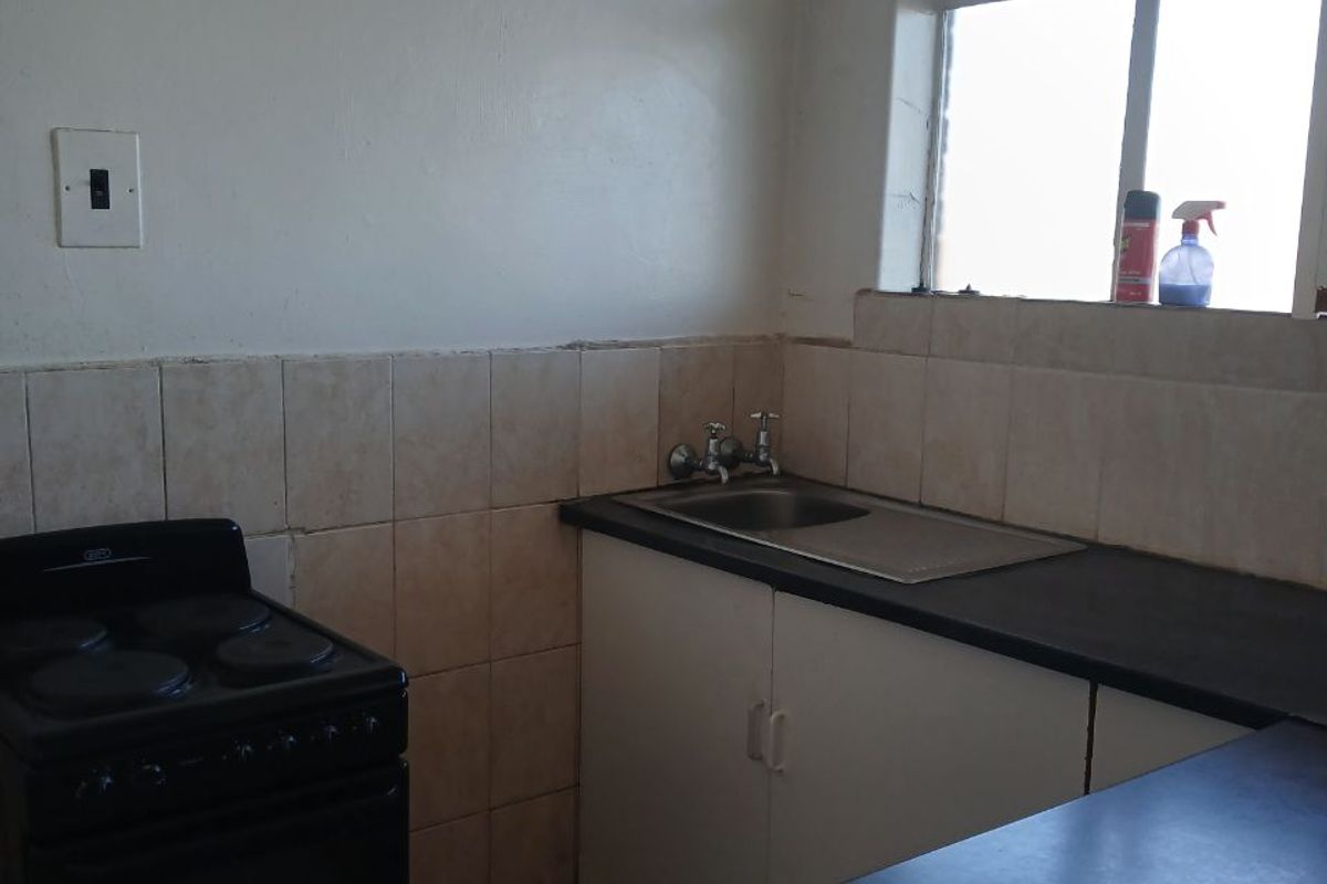 A compact kitchen featuring a stainless steel sink, tiled splashback, laminate countertops, and an electric stove, requiring some maintenance and cosmetic updates.