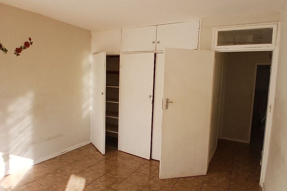 An empty bedroom featuring built-in cupboards with overhead storage, tiled flooring, and a transom window above the doorway.