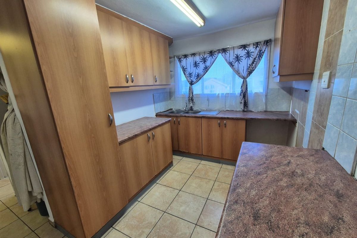A functional kitchen featuring laminate cabinetry, ample countertop space, a double bowl sink, and ceramic floor tiles, offering a practical layout for renovation.