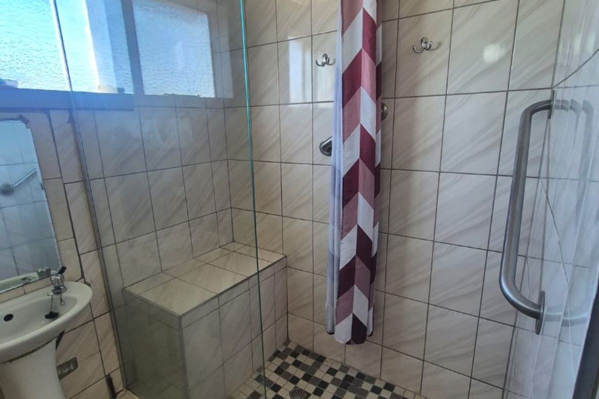 A functional bathroom featuring a walk-in shower with a built-in bench, glass screen, overhead shower rose, and a pedestal basin.