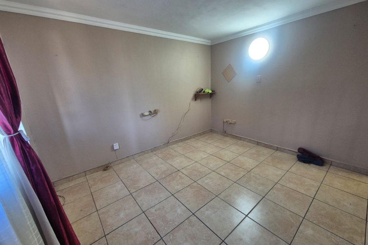 An empty bedroom featuring tiled flooring, a unique circular window, and coved ceiling detailing, ready for a fresh update.