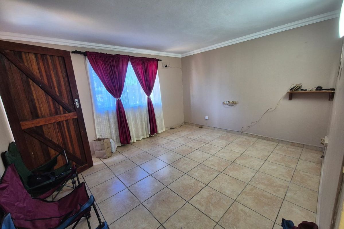 An empty living room featuring tiled flooring, a solid wooden door, and neutral wall finishes, offering a blank canvas for interior design.