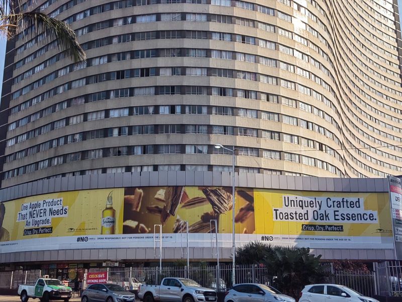 Exterior view of a large multi-story apartment building featuring a prominent advertising hoarding on the lower level.