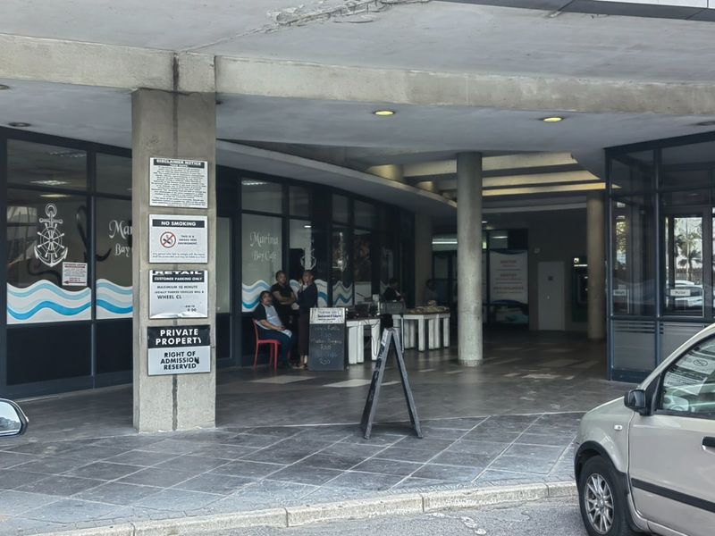 Exterior view of a commercial building entrance featuring a covered walkway, tiled flooring, and aluminium-framed glass storefronts.