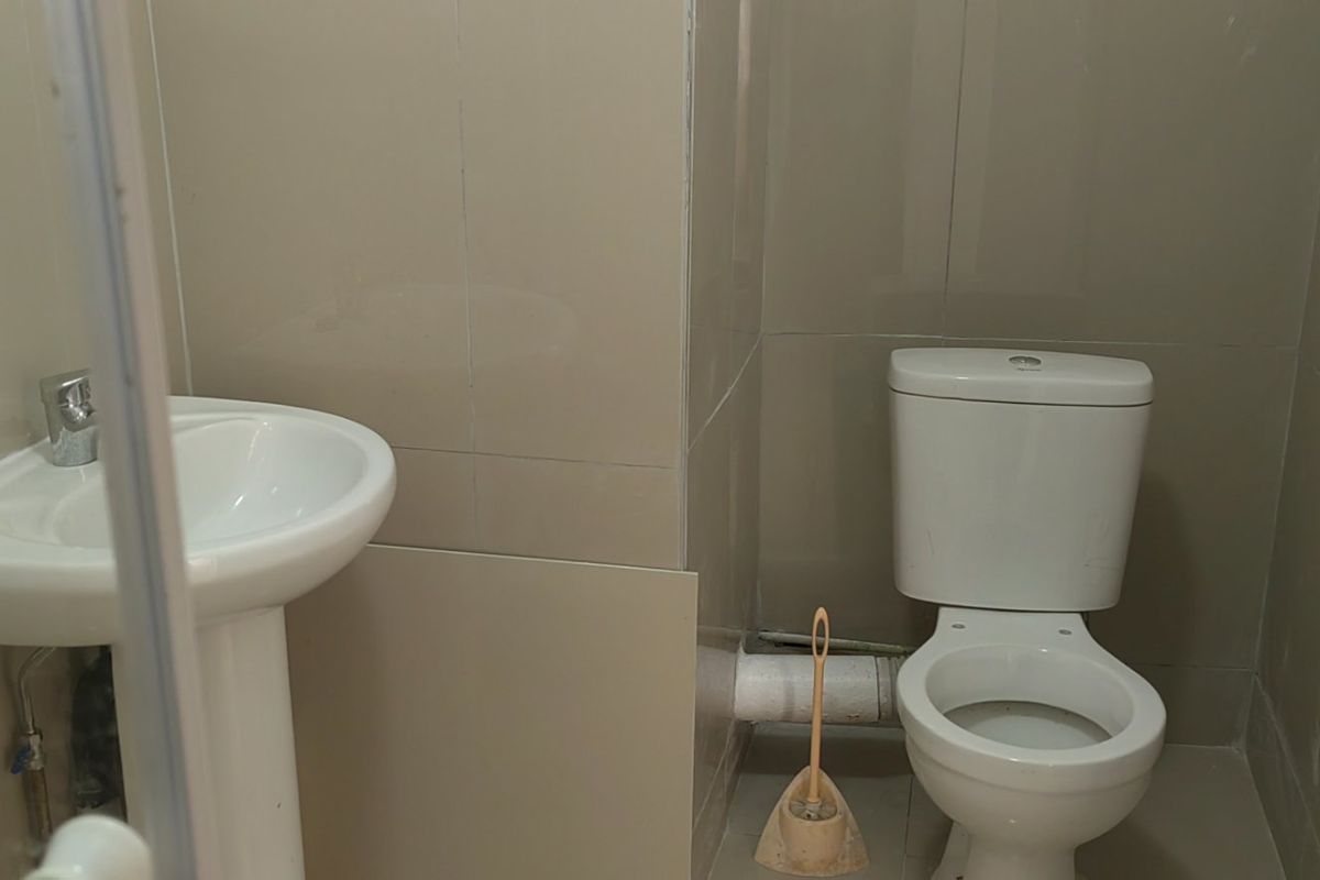 A compact bathroom featuring a pedestal washbasin and a standard toilet with full-height ceramic wall tiling.