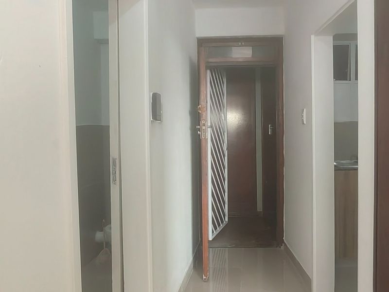 A functional apartment hallway featuring tiled flooring, built-in storage cupboards, and a security gate leading to the entrance.