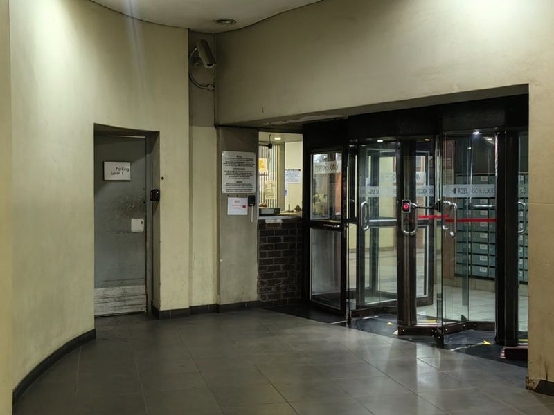 A functional apartment building entrance lobby featuring a revolving glass door, tiled flooring, and a reception area with integrated mailboxes.