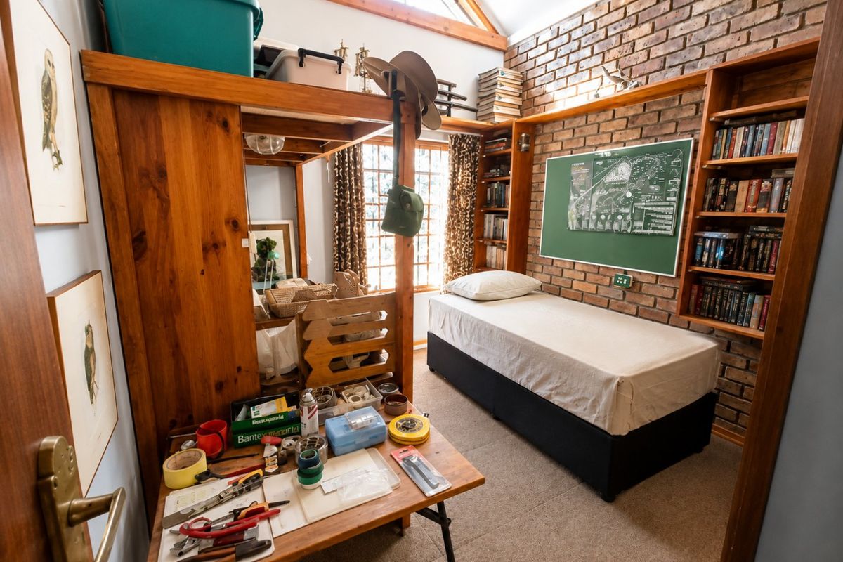 A cozy bedroom featuring exposed brick walls, built-in wooden shelving, and a vaulted ceiling with timber beams, offering a rustic and character-filled living space.