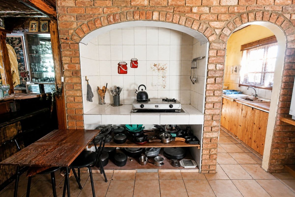 Rustic kitchen featuring a brick-arched gas hob alcove, tiled backsplash, and open shelving, with an adjacent scullery area visible through the archway.