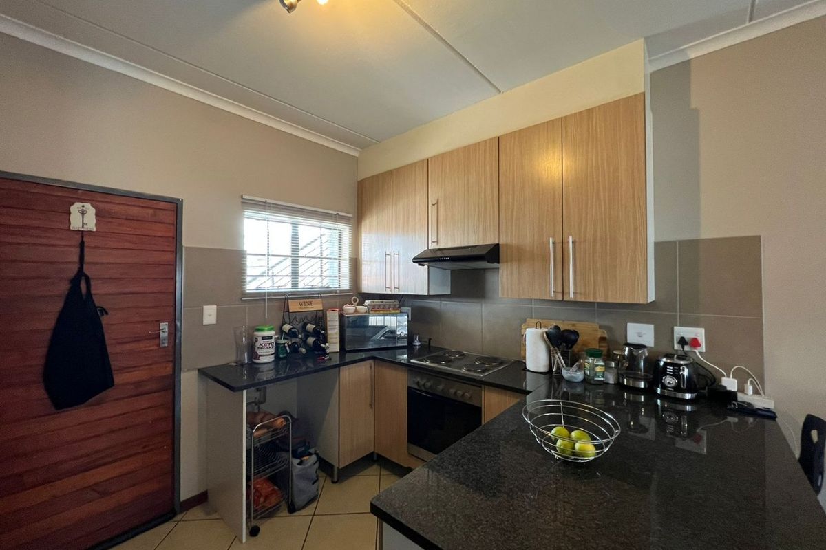 A functional kitchen featuring light wood cabinetry, dark granite countertops, built-in oven and hob, and tiled flooring with a neutral backsplash.