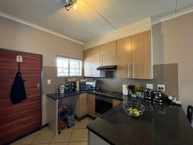 A functional kitchen featuring light wood cabinetry, dark granite countertops, built-in oven and hob, and tiled flooring with a neutral backsplash.