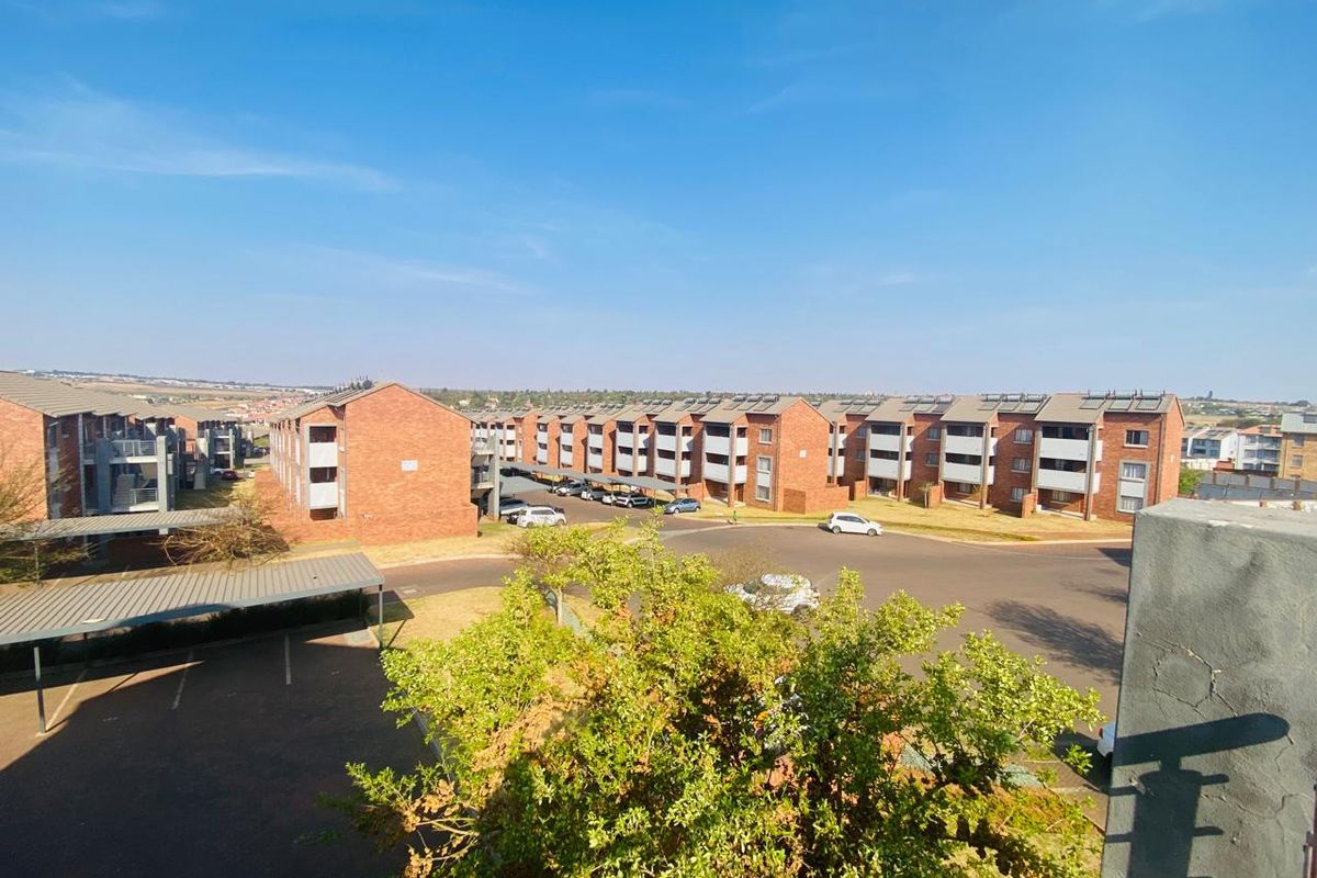 An elevated aerial view of a residential apartment complex featuring brick buildings, covered parking bays, and solar water heating installations.