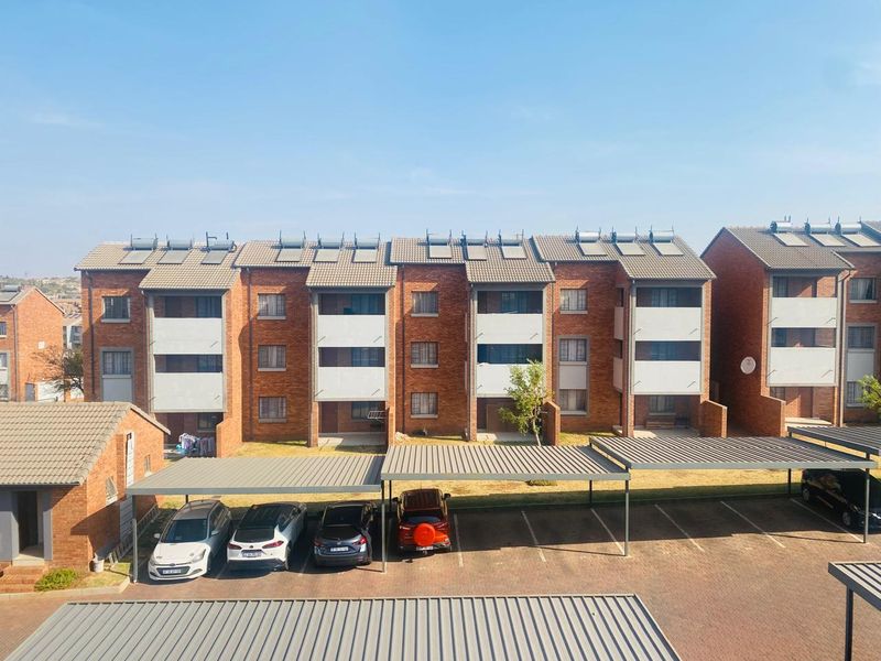 Exterior view of a multi-story face brick apartment complex featuring tiled roofs with solar panels and dedicated covered parking bays.