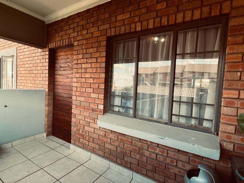 A covered balcony area featuring exposed brick walls, tiled flooring, and a large metal-framed window, providing a functional outdoor space.
