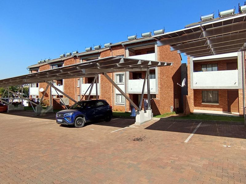 Exterior view of an apartment complex featuring brick facade buildings, covered parking carports, and solar water heating systems installed on the roof.