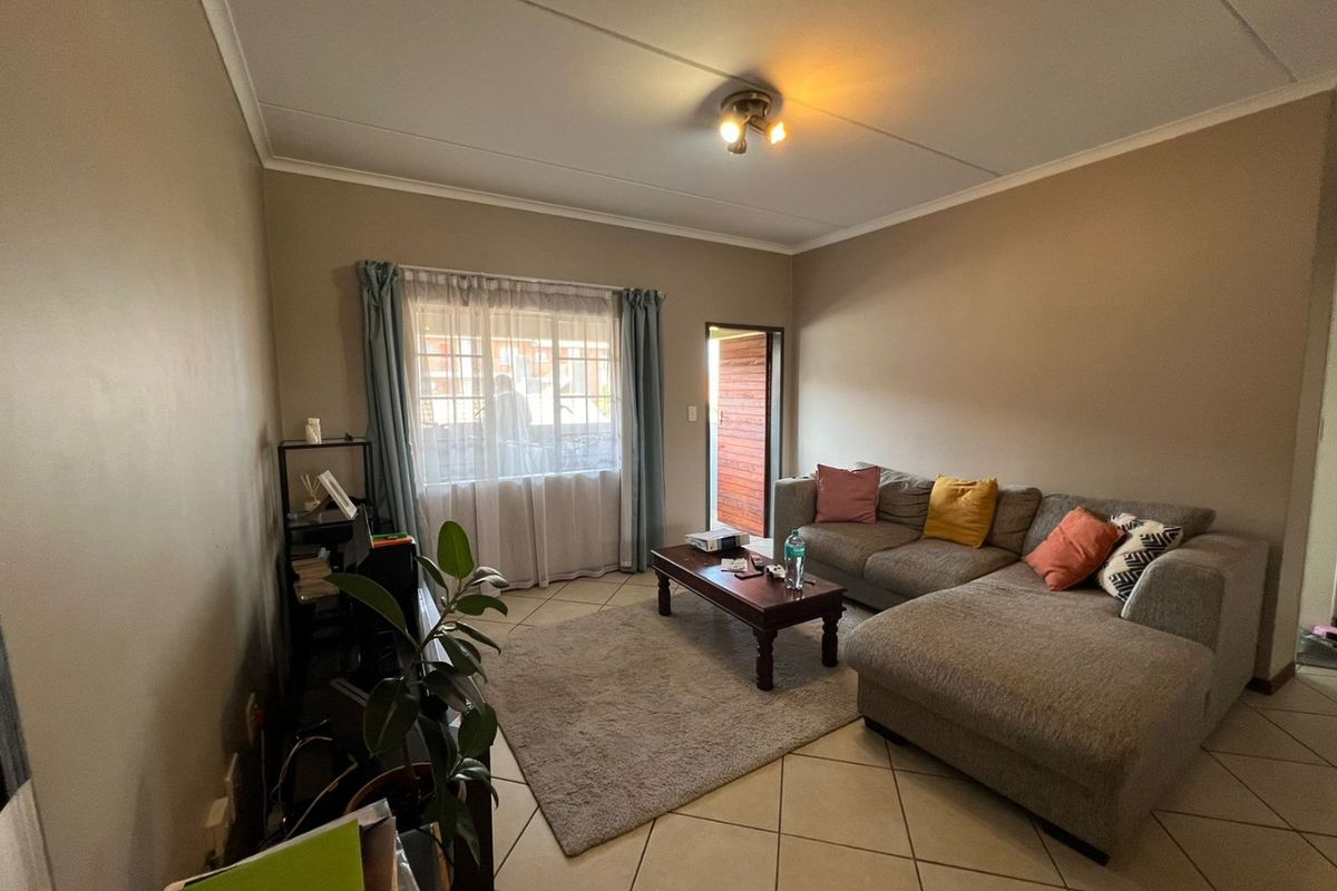 A comfortable living room featuring tiled flooring, neutral wall tones, and natural light from the window and exterior door access.