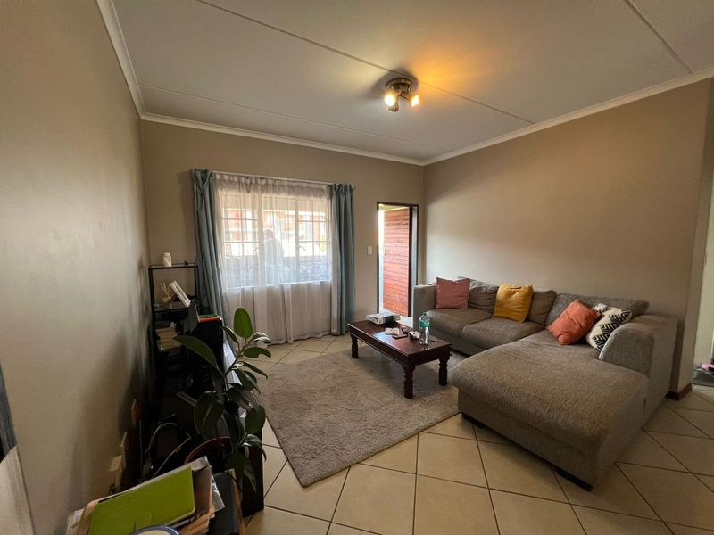 A comfortable living room featuring tiled flooring, neutral wall tones, and natural light from the window and exterior door access.
