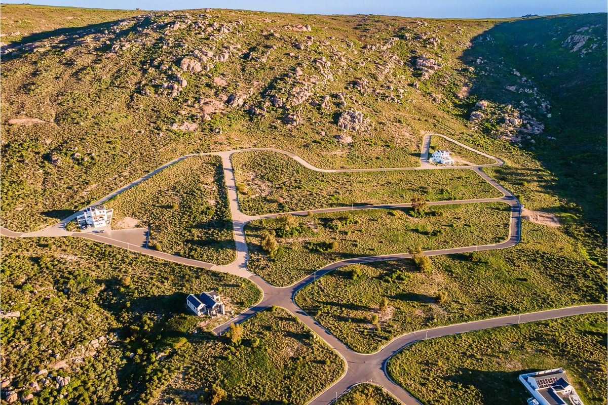 Aerial view of a residential development featuring paved roads and multiple vacant plots set against a natural hillside landscape.