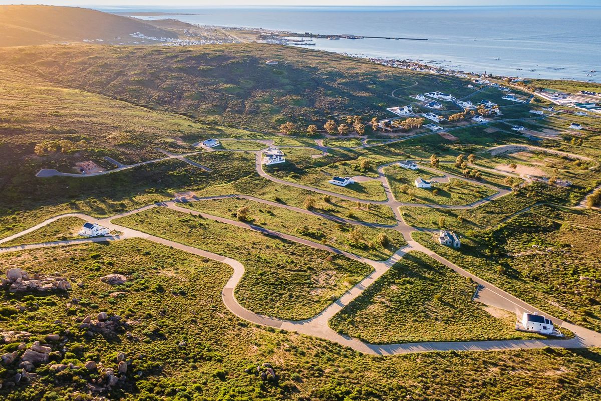 An aerial view of a coastal residential development featuring paved roads, scattered residential plots, and expansive natural landscape overlooking the ocean.