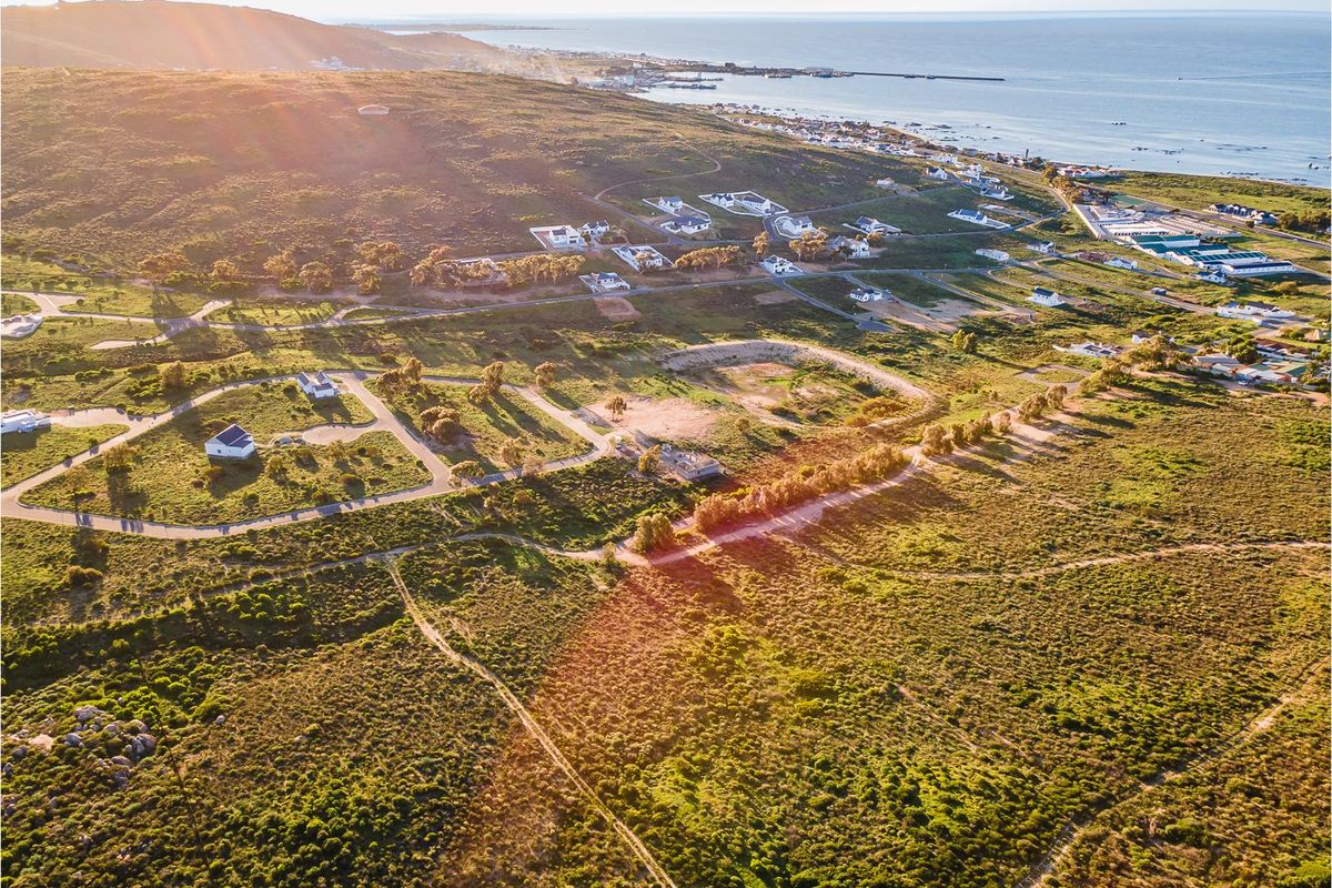 An aerial view of a coastal residential estate, showcasing the surrounding landscape, access roads, and proximity to the ocean.