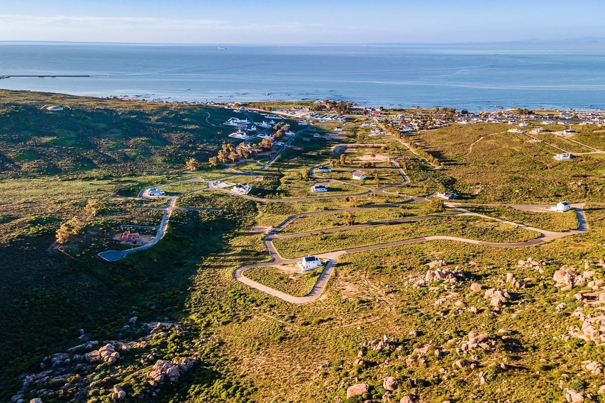 An aerial view of a coastal residential development featuring paved road infrastructure and expansive natural landscape with ocean views.