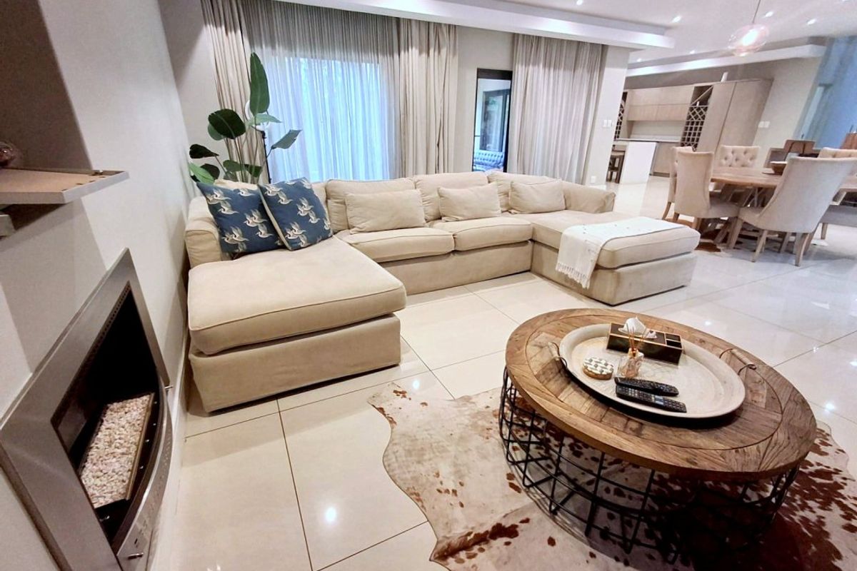Spacious open-plan living area featuring a modern built-in fireplace, polished tiled flooring, and recessed ceiling lighting, seamlessly flowing into the dining and kitchen space.