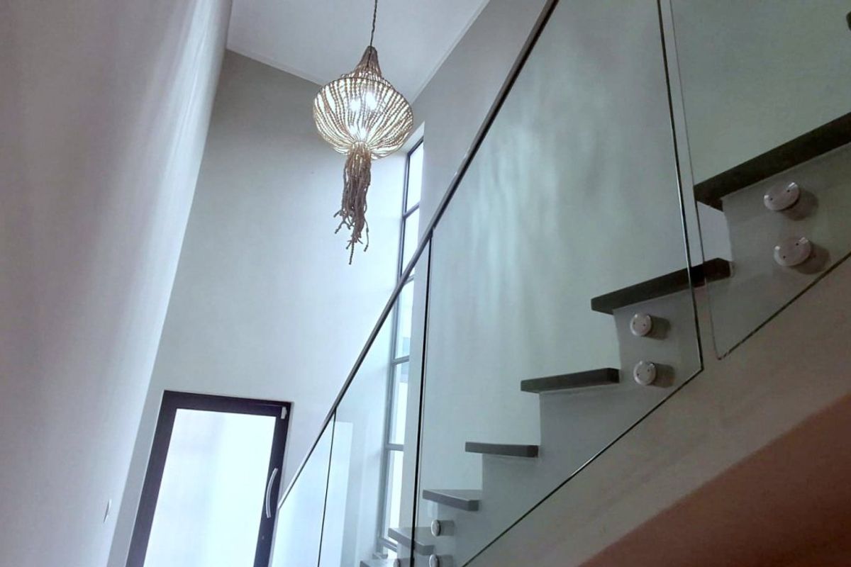 A modern staircase featuring a sleek glass balustrade, high ceilings, and a tall window that allows for ample natural light.