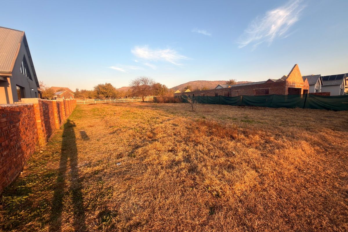 A vacant residential plot featuring a brick boundary wall and open grass area with surrounding neighborhood views.