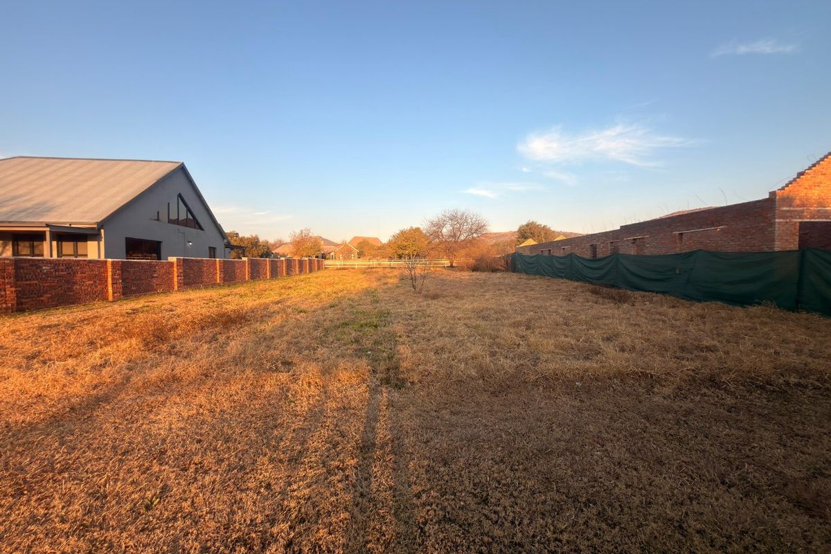 A vacant residential plot featuring dry grass, enclosed by brick boundary walls and temporary fencing, offering a clear space for future development.