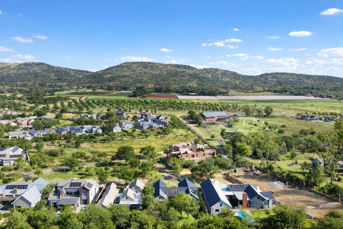 An elevated aerial view of a residential estate featuring modern homes, landscaped surroundings, and scenic mountain views in the background.