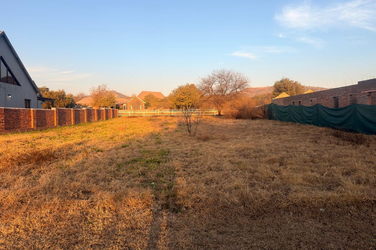 A vacant residential plot featuring dry grass, enclosed by brick boundary walls and perimeter fencing with privacy screening.