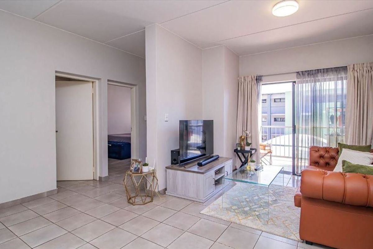 A bright living room featuring neutral tiled flooring and a sliding glass door providing direct access to an outdoor balcony.