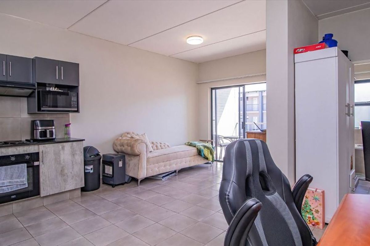 Open-plan living area featuring a compact kitchen with built-in cabinetry, oven, and extractor fan, leading to a balcony through sliding glass doors.