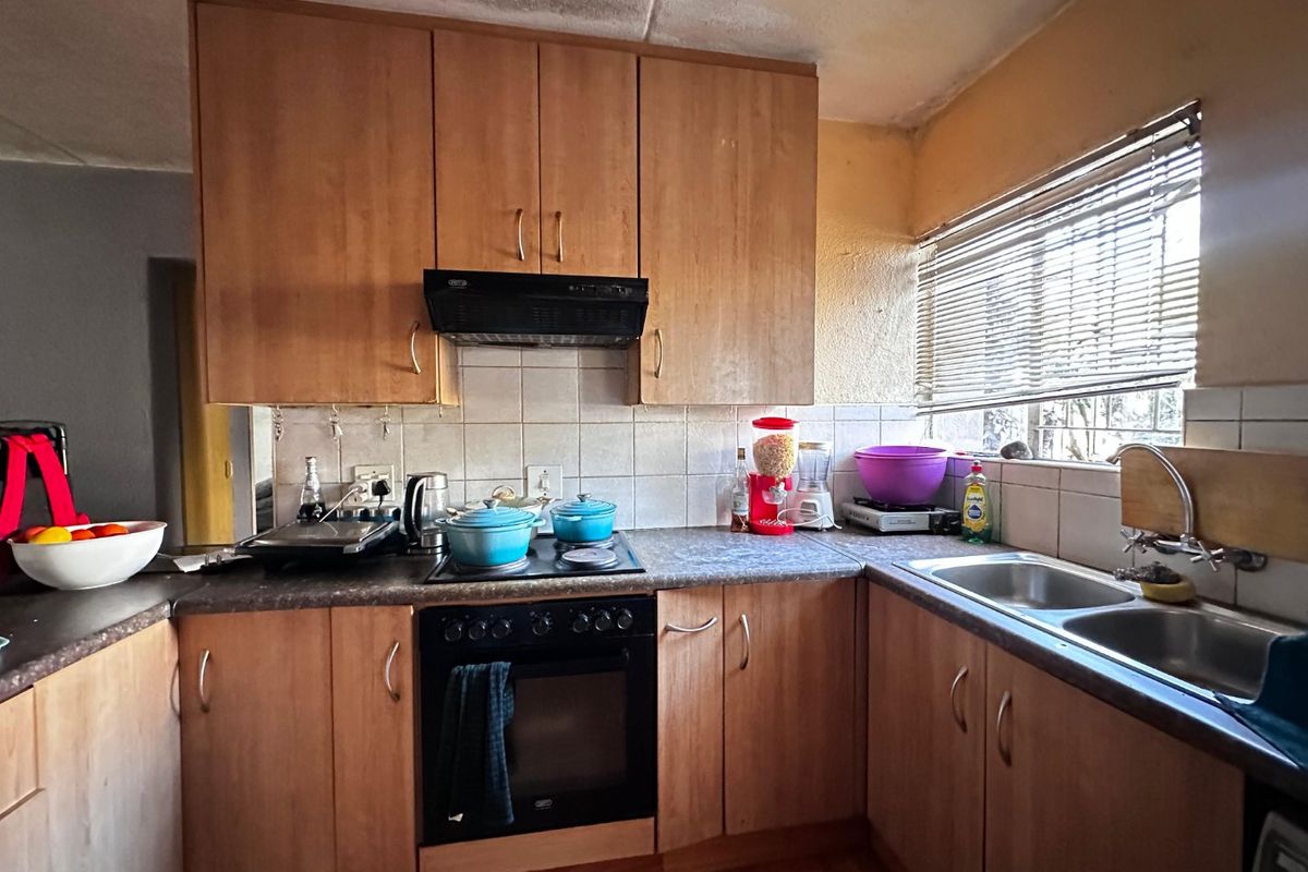 A functional kitchen featuring laminate cabinetry, built-in oven, electric hob, and a double bowl stainless steel sink with tiled backsplash and window blinds.