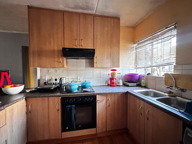 A functional kitchen featuring laminate cabinetry, built-in oven, electric hob, and a double bowl stainless steel sink with tiled backsplash and window blinds.