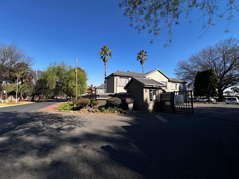 Front entrance view of the apartment complex featuring a secure gated access point, guard house, and paved driveway.