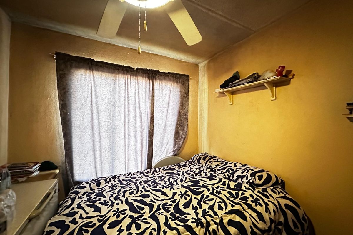 A compact bedroom featuring a ceiling fan and a built-in wall shelf, showing signs of wear on the walls and ceiling.