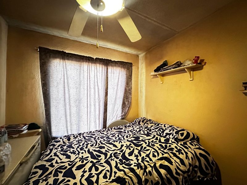 A compact bedroom featuring a ceiling fan and a built-in wall shelf, showing signs of wear on the walls and ceiling.