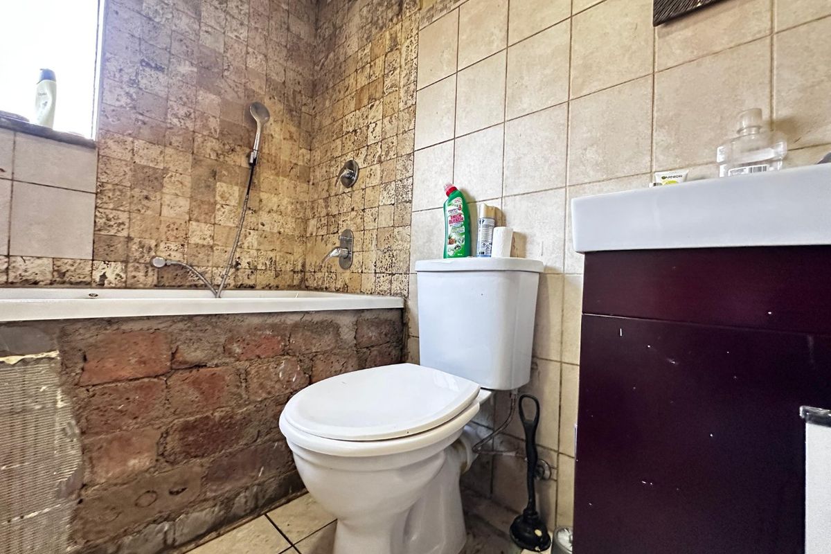 A bathroom featuring a bathtub with exposed brickwork, a toilet, and a vanity basin. The space requires renovation to finish the bathtub apron.