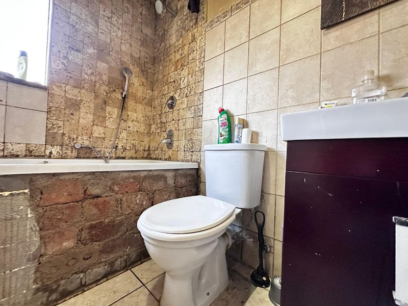 A bathroom featuring a bathtub with exposed brickwork, a toilet, and a vanity basin. The space requires renovation to finish the bathtub apron.