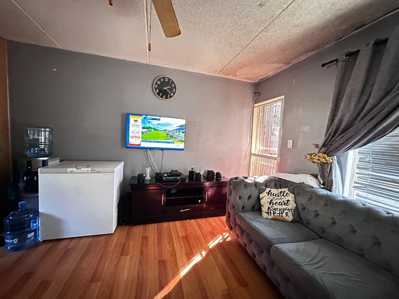 Living room featuring laminate flooring, a ceiling fan, and security gate access. The space requires cosmetic attention to the ceiling finishes.