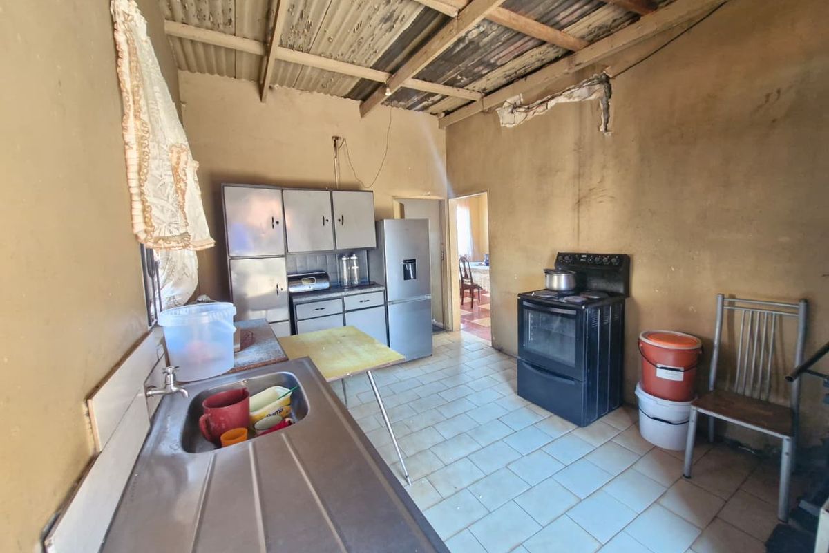 A functional kitchen space featuring tiled floors, fitted cabinetry, and an exposed timber roof structure, currently requiring significant renovation and cosmetic updates.