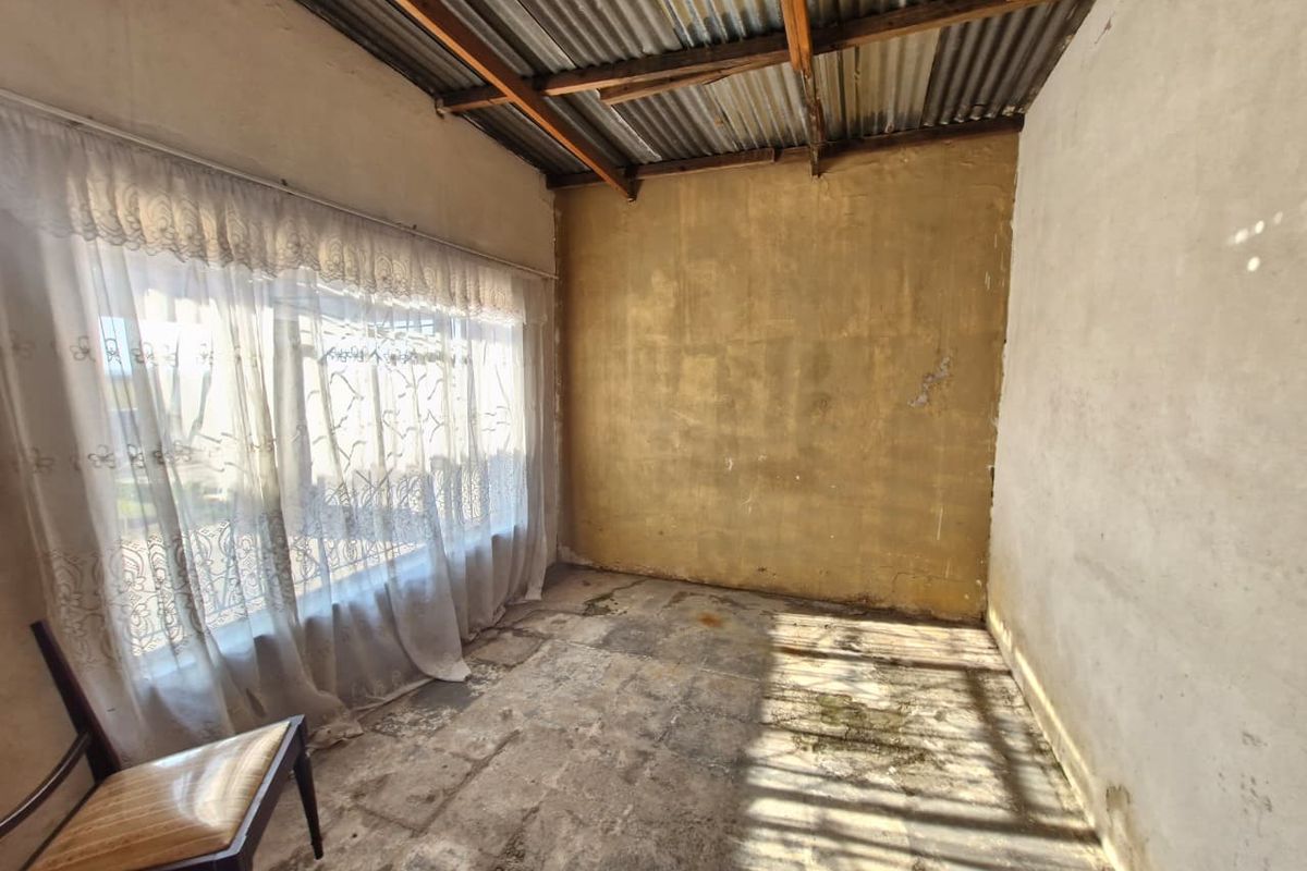 A vacant bedroom space featuring exposed timber rafters, corrugated iron roofing, and concrete flooring, requiring significant renovation and cosmetic updates.
