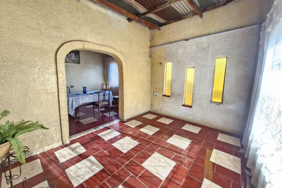 A spacious living area featuring unique arched entryways, decorative tiled flooring, and exposed roof rafters, offering a blank canvas for renovation.