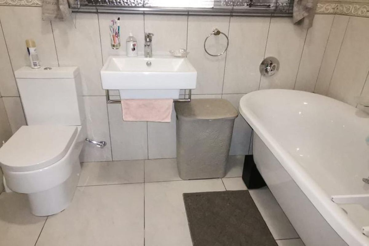 A functional bathroom featuring a wall-mounted basin, a modern toilet, and a classic freestanding bathtub with full-height wall tiling.