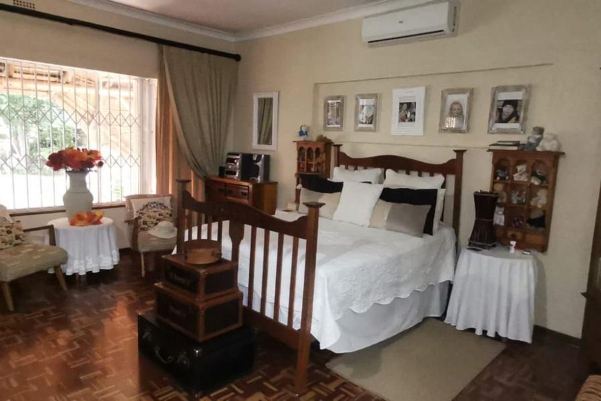 A spacious bedroom featuring parquet flooring, a wall-mounted air conditioning unit, and large windows with security bars.